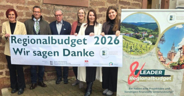 Gruppe von sechs Personen hält ein Banner „Regionalbudget 2026 – Wir sagen Danke“ vor einer Sandsteinwand; daneben ein Roll-Up mit Landschaftsfotos.