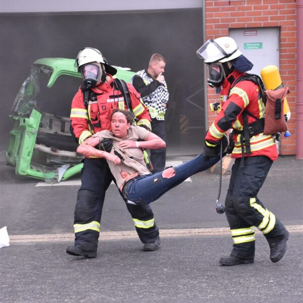 Feuerwehrkräfte unter Atemschutz tragen bei der Übung eine als verletzt geschminkte Darstellerin aus dem Gebäude